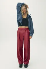 Pantalón de cuero sintético color bordó, de tiro medio, corte recto y cintura cruzada con trabillas. Cuenta con bolsillos laterales, pinzas delanteras y cierre frontal con cremallera, botón y gancho metálico.