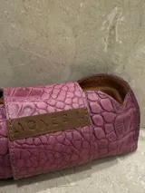 Estuche para lentes con textura símil cocodrilo color azul y cierre con tira de cuero marrón con el logo de la marca.