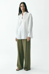 Camisa blanca con rayas verticales, cuello solapa, manga larga y cierre frontal con botones.