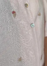 Blusa color rosa pálido de lino con bordados de motivos marinos, escote en V, mangas cortas abullonadas y cierre frontal con botones.