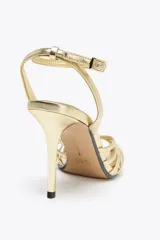 Sandalias de tacón alto fino color dorado, con tiras finas entrecruzadas y cierre con hebilla en el tobillo.