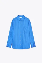 Camisa celeste con rayas verticales blancas, de corte oversize, cuello solapa, manga larga con puños y bolsillo de plastrón en el pecho.