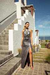 Vestido largo plateado de lamé elastizado, con escote halter, cuello con lazo y tajo lateral.