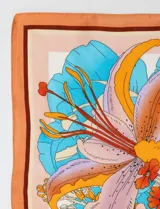 Pañuelo cuadrado de satén estampado con diseño floral en tonos naranja, celeste y lila.