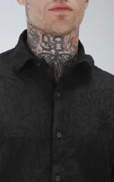 Camisa negra de manga corta con textura floral en relieve y cuello clásico.