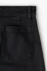 Jean de denim de algodón negro con leve stretch, pierna ancha, corte ajustado de cintura a cadera y holgado de muslo a bajo. Tiene cintura de tiro alto con cierre y botón, y bolsillos de parche delanteros y traseros.