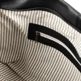 Bolso tipo tote de cuero negro con asas fijas, acceso con cierre y herrajes dorados. Interior forrado en algodón y poliéster con un bolsillo con cierre y dos abiertos.