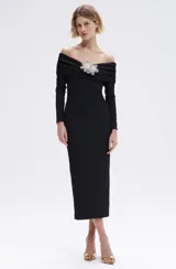 Vestido midi negro de hombros descubiertos confeccionado en punto merian con forro en el cuerpo, presenta bordado de flores 3D en la parte delantera, canesú en el escote con volantes en los laterales y en el centro delantero y una abertura en la espalda.