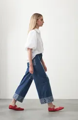Pantalón de denim azul oscuro con bordado estilo bandana en blanco en los laterales de las piernas y en los puños. El corte es recto y amplio, llegando al tobillo.