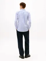 Camisa de hombre Tommy Hilfiger de corte regular, confeccionada en tejido Oxford de algodón con textura y diseño a rayas verticales azules y blancas. Cuenta con cuello abotonado, mangas largas con puños abotonados y logo bordado en el pecho.