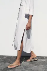 Vestido camisero largo color verde claro, confeccionado en lino. Tiene cuello solapa, escote en V, manga tres cuartos con trabilla y botón, bolsillos delanteros de plastrón, aberturas laterales en el ruedo y cierre frontal con botones.