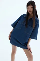 Vestido corto de denim azul, con cuello camisero, escote en V, manga corta y dos bolsillos de parche en el pecho.