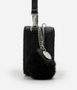 Cartera negra tipo camera bag con textura en relieve, correa de mano, asa desmontable y pompón colgante.
