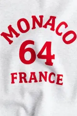 Buzo gris melange oversized con cuello redondo ribeteado acanalado y diseño de texto en rojo con la leyenda "Monaco 64 France". Modelo con hombros caídos y remate acanalado en puños y bajo. Interior cepillado suave.