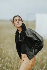 Campera de cuero negra con solapa amplia de corderito negro, de calce oversize y mangas anchas con detalle de cuero trenzado en la parte delantera.