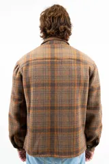 Camisa leñadora a cuadros marrón y naranja, forrada en corderito sintético, con cuello clásico, cierre frontal con botones, dos bolsillos frontales con tapa y puños abotonados.