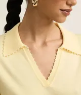 Blusa de punto color blanco, con cuello polo, escote en V y mangas cortas. Detalle de mini perlas aplicadas en el cuello.