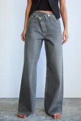 Pantalón de jean celeste de tiro alto, corte wide leg y largo hasta el tobillo. Presenta un diseño asimétrico en la cintura con cierre frontal cruzado con cremallera y botones metálicos.