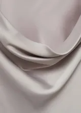 Vestido corto color gris plateado de tejido satinado, con cuello drapeado y mangas largas.