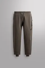 Pantalón jogger color marrón oscuro, corte regular fit, confeccionado en tejido técnico compacto de algodón con elasticidad. Cuenta con cintura elástica ajustable con cordón, bolsillos frontales y bolsillo lateral con cierre de cremallera.