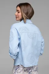 Campera corta color coral con cuello camisero, cierre frontal con botones, bolsillos de parche en el pecho y mangas largas con puños abotonados. Presenta calados tipo broderie en hombros, mangas y espalda.