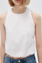 Blusa blanca de algodón sin mangas, con cuello a la base, abertura en la espalda y lazo ajustable.