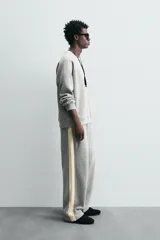 Pantalón de jogging gris con corte relaxed fit, cintura elástica ajustable con cordón interior, bolsillos laterales y traseros de vivo, y banda lateral color crema.