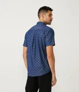 Camisa de manga corta azul con estampado de círculos blancos, cuello camisero, abotonada al frente y con bolsillo en el pecho.
