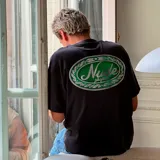 Camiseta gris con estampado ovalado en la espalda con el logo de la marca Nude Project en color verde.