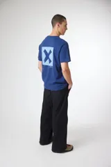 Remera de manga corta color gris oscuro, con cuello redondo y un pequeño parche cuadrado con una 'X' estampada en el pecho izquierdo.