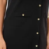 Vestido corto negro de punto grueso con botones dorados al frente, cuello redondo y mangas cortas. Presenta bolsillos de parche a la altura del busto y en la falda.