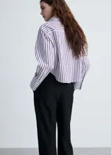 Camisa crop de rayas verticales blancas y azules, con cuello camisero, cierre frontal con botones, mangas largas con puños abotonados y corte regular.