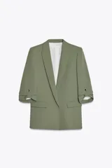 Blazer color verde oliva, de corte recto, con cuello solapa y hombreras. Tiene mangas 3/4 con trabilla y botón dorado para remangar, y bolsillos delanteros con solapa.