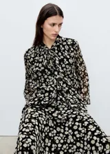 Blusa de gasa negra con estampado de margaritas blancas, cuello pico con lazo y cierre de botones frontal.