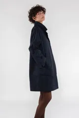 Gabardina color beige de largo medio con corte regular, fabricada en nailon repelente al agua. Tiene costuras interiores con ribete de nailon, cierre frontal con botones ocultos, escote medio bajo con cuello solapa, puño ancho con ventilación, manga de una pieza con costura en el puño, bolsillo de ribete inclinado y parche de logotipo de silicona.