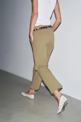 Pantalón cropped color beige de tiro alto y corte recto, confeccionado en algodón. Cuenta con bolsillos delanteros y traseros, trabillas en la cintura y cierre frontal con cremallera y botón.