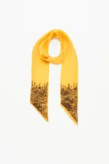 Pañuelo largo y angosto tipo corbatín de símil seda color amarillo mostaza, con detalle de lentejuelas bordadas en los extremos en tonos oscuros.