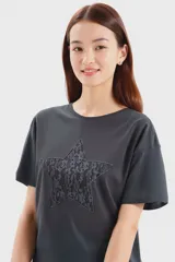 Remera gris topo de corte holgado con cuello redondo y mangas cortas. Presenta una estrella central con aplique de encaje.