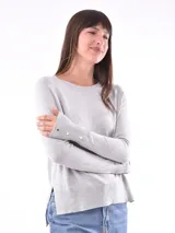 Buzo de tejido de punto color gris claro, con cuello redondo y manga larga. Presenta detalles de botones dorados en los puños.