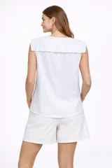 Blusa blanca sin mangas con cuello Peter Pan grande con volados en el borde. Cierre frontal con botones.