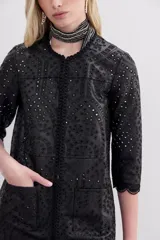 Saco negro de símil cuero con bordado de flores y calado en toda la prenda. Tiene cuello redondo, mangas largas y apertura frontal con broches ocultos.