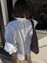 Blusa blanca de lino con cuello alto fruncido, mangas 3/4 con volados y detalle constructivo en el delantero con costuras a mano.