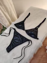 Conjunto de bikini negro de cuerina texturizada, con corpiño triangular con aro metálico central y bombacha colaless con tiras laterales ajustables.