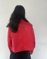 Campera roja de cuero sintético, con cuello solapa, cierre cruzado con botones a presión y cinturón con hebilla.