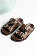 Sandalias marrones de cuero con dos tiras con hebillas ajustables y detalle de tachas plateadas.