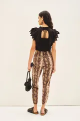 Pantalón estilo babucha con estampado de piel de serpiente en tonos marrones y beige. Posee cintura elástica con cordón de ajuste, puños ajustables en los tobillos y detalles metálicos.