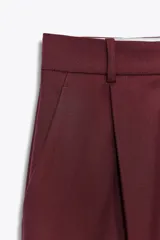 Pantalón de vestir color borgoña, de tiro alto y pierna ancha, con bolsillos laterales y cierre frontal con cremallera y ganchos metálicos.