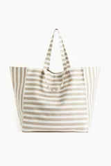 Bolso de playa tipo tote bag, de lona de algodón a rayas horizontales color beige y blanco. Tiene doble asa de hombro y un compartimento interior.