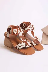 Sandalias con estampado de vaca en tonos marrones y blancos, con hebilla ajustable y tacón bajo de madera.