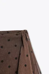 Falda pantalón corta color marrón con estampado de lunares negros, tiro medio, volantes y cierre lateral con cremallera.